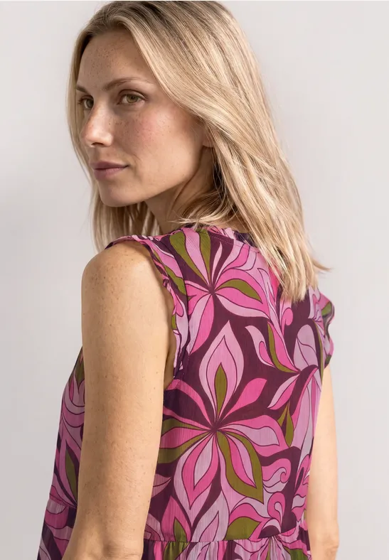 Vrouw van achteren in mouwloze top met roze-paarse bloemenprint, schouderlang blond haar.