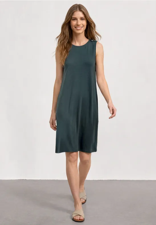 Femme en robe d'été sans manches, longueur genou, couleur gris-vert, sandales plates, fond neutre.