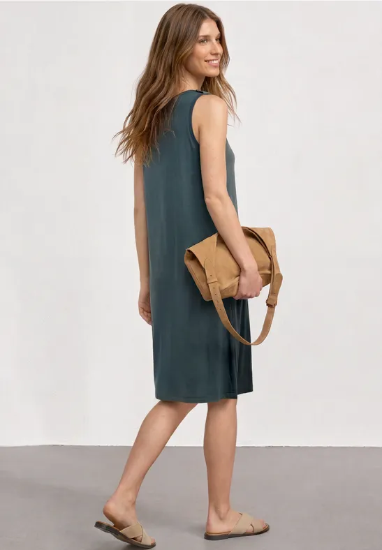 Femme de profil en robe grise sans manches, sandales plates et sac bandoulière bicolore.