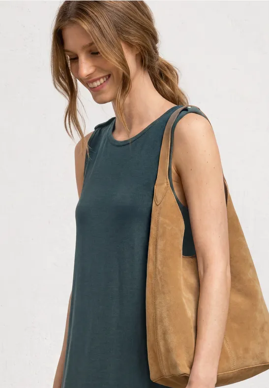 Une femme porte un top sans manches sombre et un grand sac bandoulière en daim marron clair.