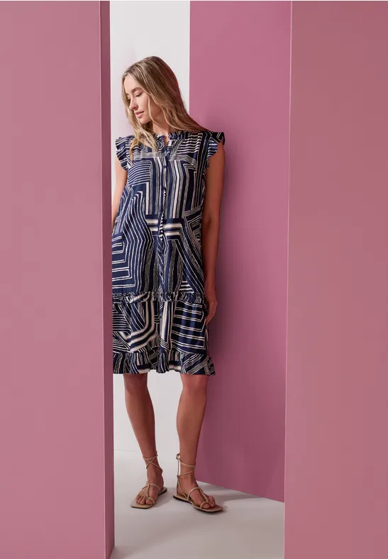 Frau in blau-weiß gemustertem Kleid vor rosa Wänden.