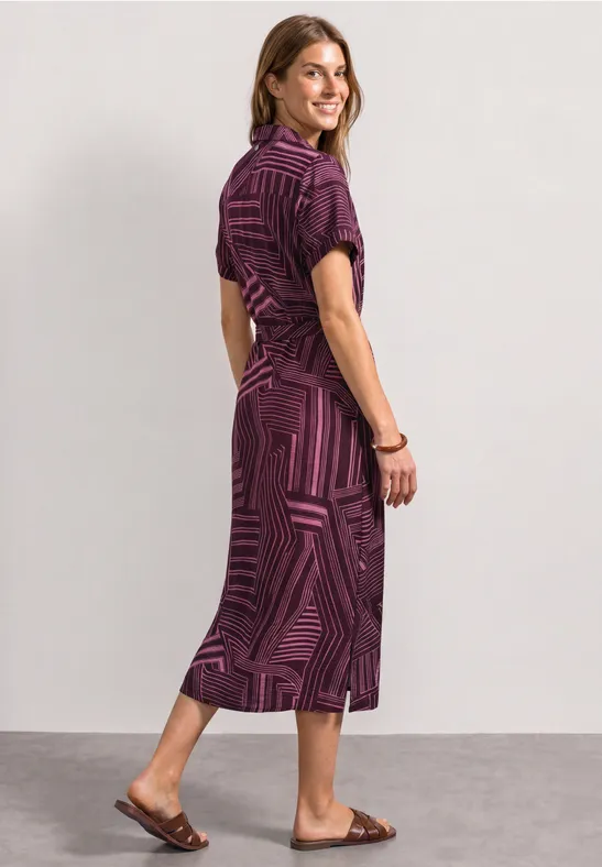 Vrouw in een paarse, gemêleerde midijurk met platte sandalen.