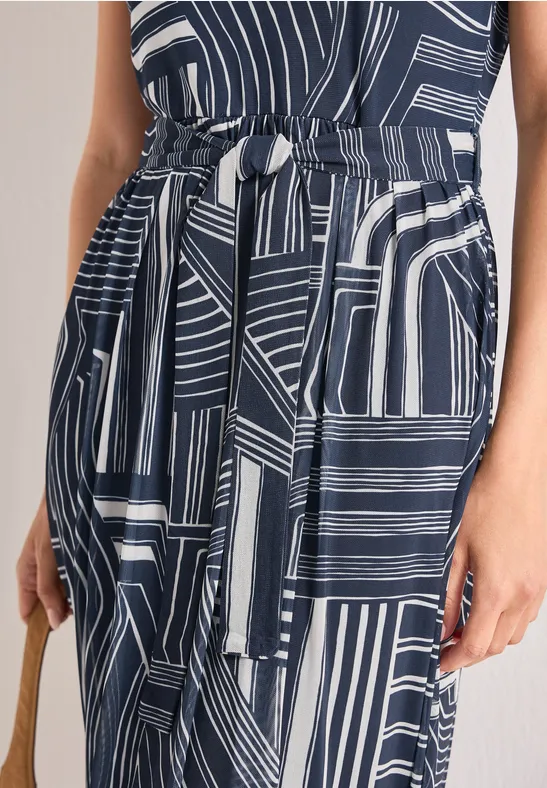 Close-up van een donkerblauwe jurk met witte geometrische strepen, een tailleband en een tas.