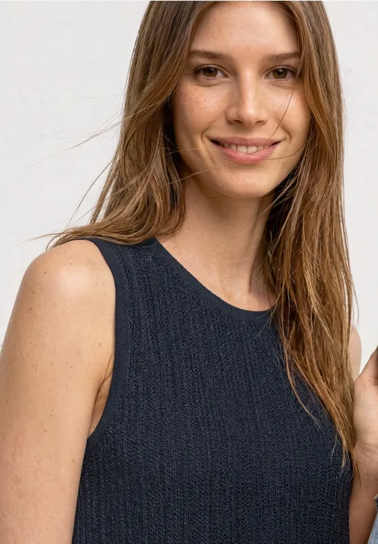 Een vrouw draagt een mouwloze zwarte top, frontaal zicht op bovenlichaam, gezicht onscherp.