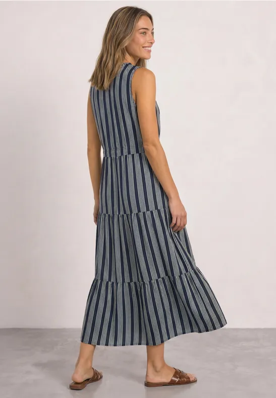 Frau trägt ärmelloses, gestreiftes Maxikleid in Blau und Weiß mit Stufenrock und flachen Sandalen.