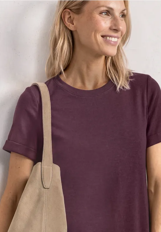 Vrouw met blond haar draagt een paarse t-shirt en een beige tas.