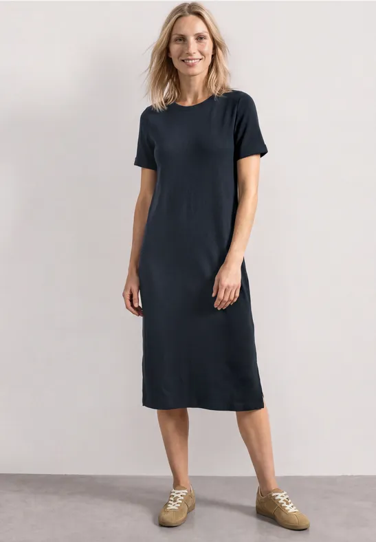 Een vrouw draagt een simpel donkerblauw midi-T-shirtjurk met lichte sneakers.
