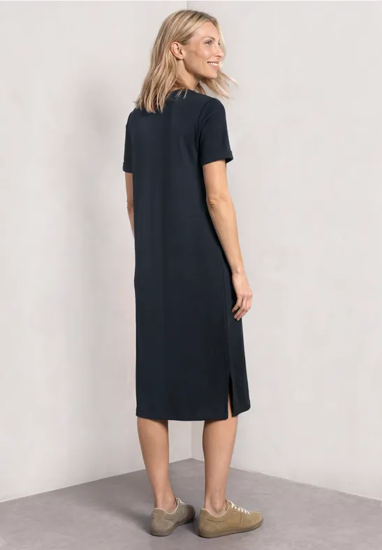 Vrouw met een eenvoudig zwart T-shirtjurk tot over de knieën, korte mouwen en zijslitsen.