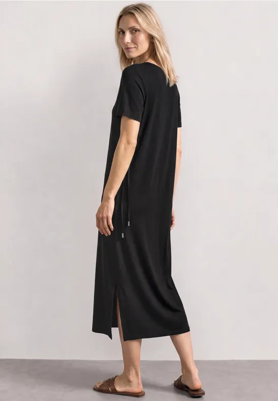 Femme porte une robe T-shirt noire mi-longue, manches courtes et fentes sur les côtés.