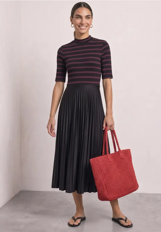 Frau in gestreiftem Oberteil, schwarzem Plisseerock, schwarzen Sandalen und rotem Shopper