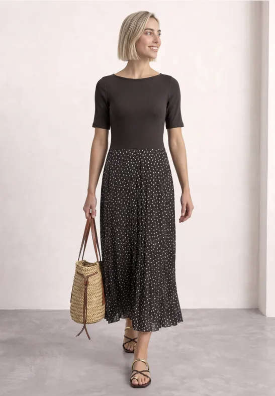 Femme blonde porte un top noir et une jupe à pois, sandales et panier en paille.