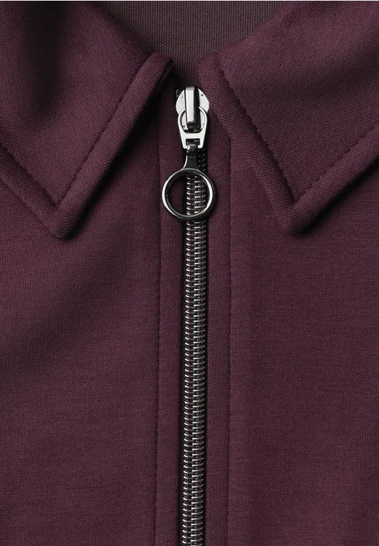 Nahaufnahme eines weinroten Kleidungsstücks mit Reißverschluss und rundem Zipper-Anhänger.