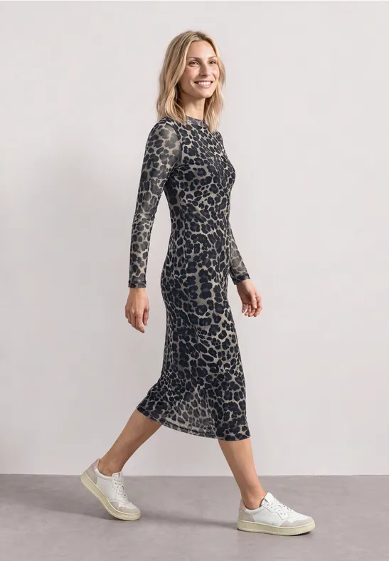 Eine Frau in seitlicher Pose trägt ein knielanges, langärmeliges, gemustertes Kleid und weiße Sneaker.