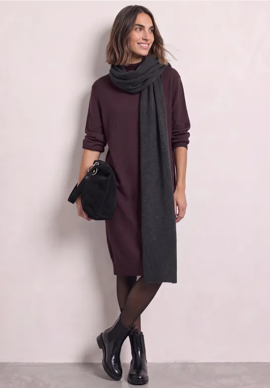 Femme en robe bordeaux, long foulard gris foncé, bottines noires et sac à main.