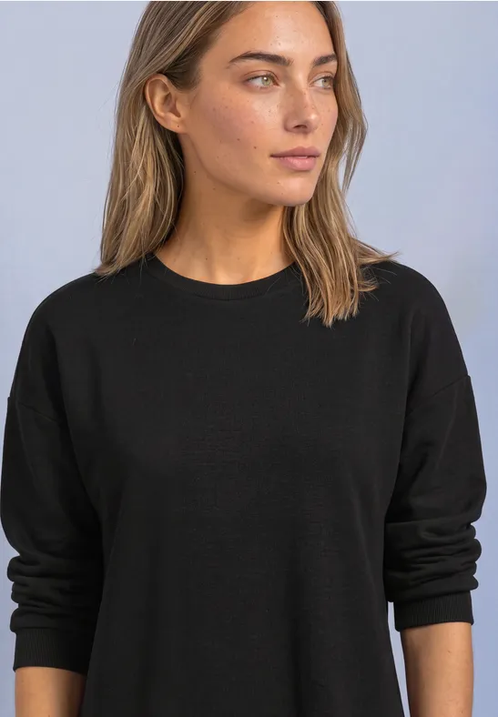 Femme en pull noir uni regardant sur le côté, fond neutre.