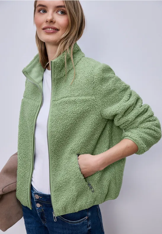 Person trägt eine hellgrüne Fleecejacke mit Reißverschluss und weißem Shirt.