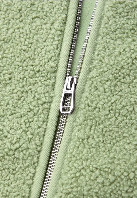 Nahaufnahme eines hellgrünen Sherpa-Fleecejacken-Reißverschlusses aus silbernem Metall.