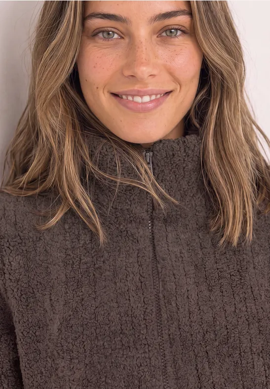 Portrait d'une femme souriante aux cheveux bruns et taches de rousseur, portant un pull brun foncé zippé.