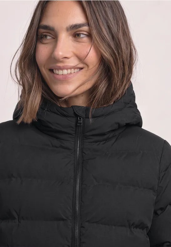 Une femme souriante porte une doudoune noire matelassée avec capuche.