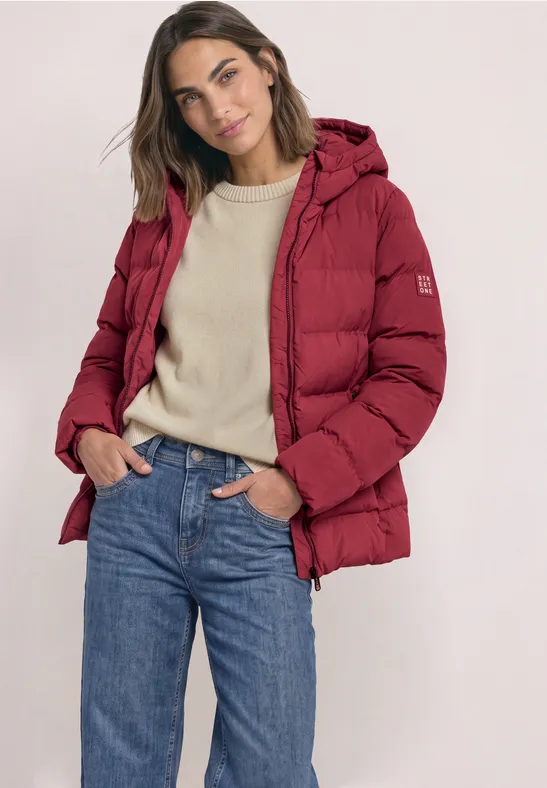 Femme en doudoune rouge, t-shirt beige et jean bleu sur fond clair.