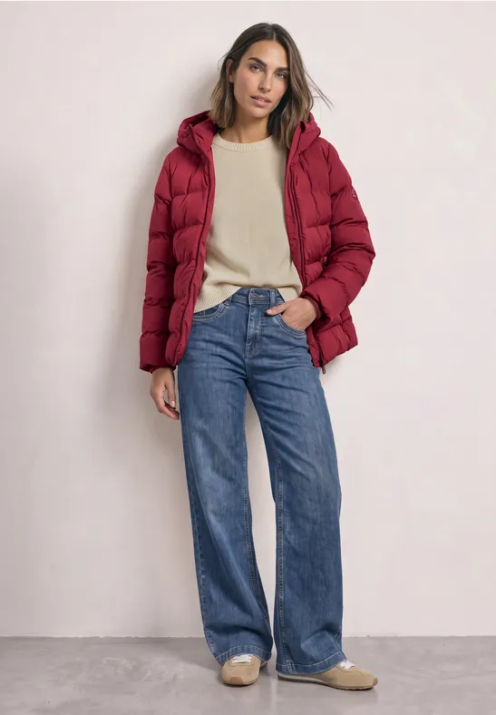 Femme en doudoune rouge, pull beige, jean large bleu et chaussures beiges sur fond neutre.