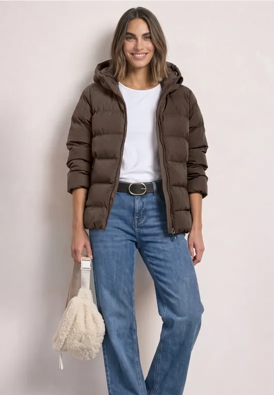 Frau im braunen Steppmantel, weißem T-Shirt, blauen Jeans und flauschiger Tasche.