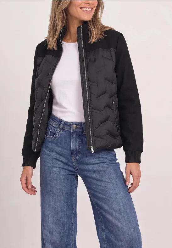 Femme en veste bomber matelassée noire, T-shirt blanc et jean bleu.