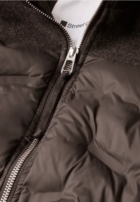 Schwarze Steppjacke mit mittig laufendem Reißverschluss und Blick auf ein weißes Shirt darunter.