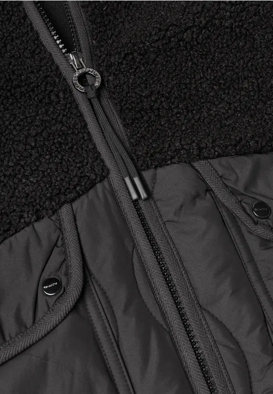 Nahaufnahme eines schwarzen Jackenoberteils mit Teddy-Fleece, Nylonpasse und durchgehendem Reißverschluss.