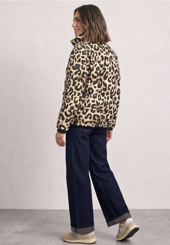 Frau trägt Leoprint-Jacke, weite Jeans und Turnschuhe vor hellem Hintergrund.