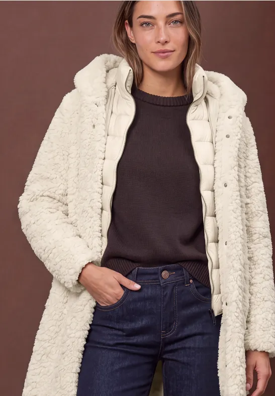 Frau in dunklem Pullover und Jeans mit cremefarbener, flauschiger Wattierung und Kapuze