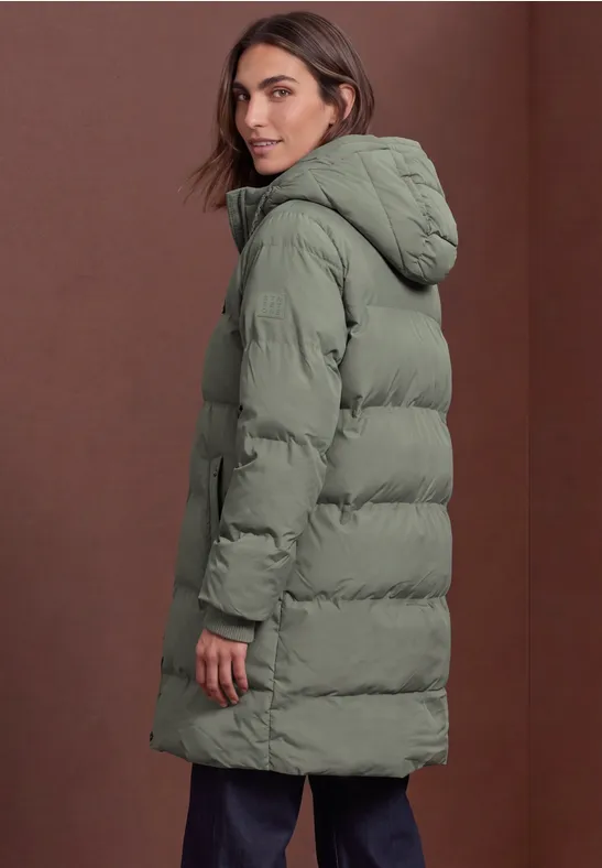 Eine Frau trägt eine lange, olivgrüne Steppjacke mit Kapuze, Rückansicht seitlich.