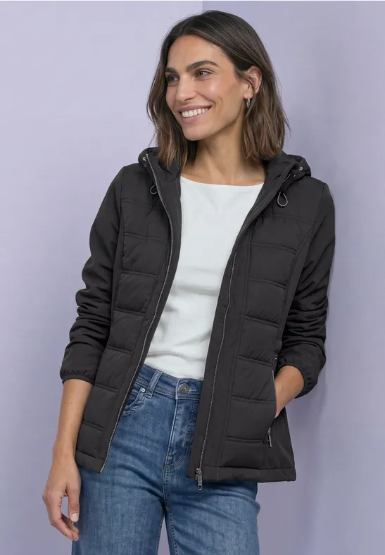 Femme en doudoune noire à capuche, t-shirt blanc et jean bleu, souriante.