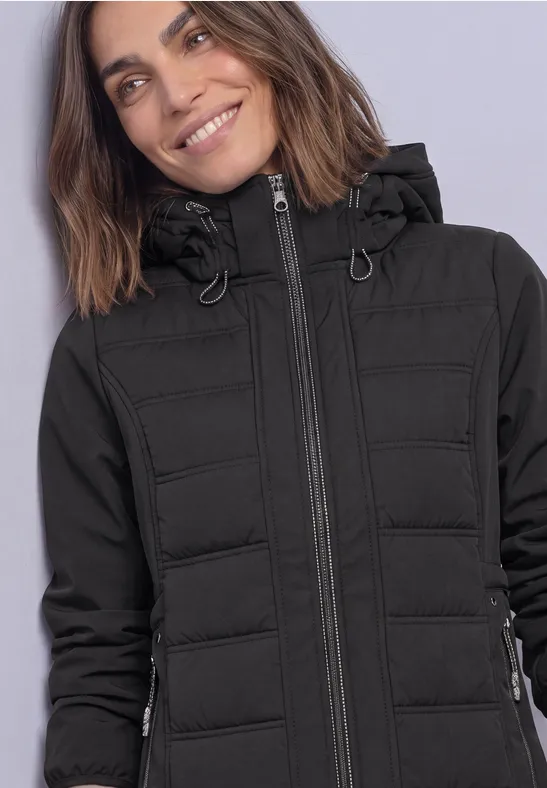 Femme souriante portant une veste matelassée noire à capuche.