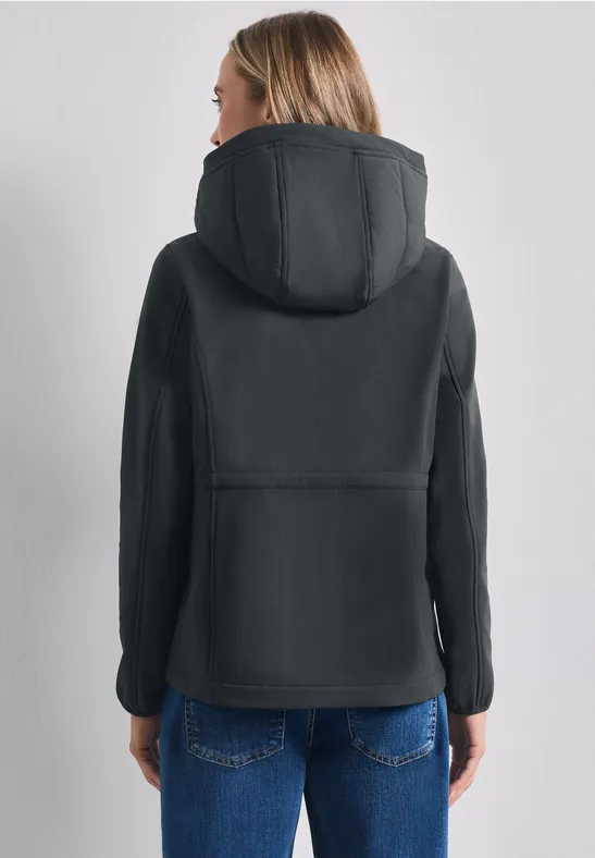 Vue de dos d’une femme portant une veste matelassée noire à capuche et un jean bleu.