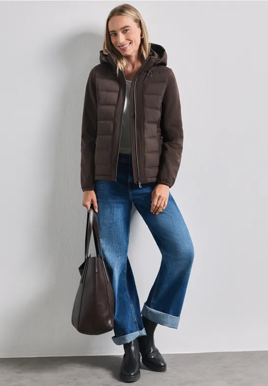 Femme en doudoune marron foncé à capuche, jean large retroussé, bottines noires et grand sac.