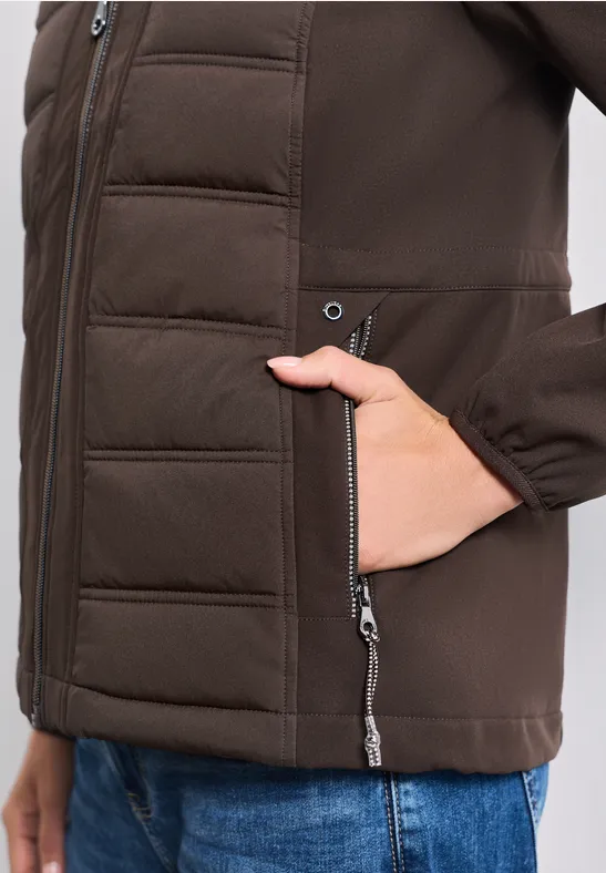 Veste matelassée marron avec poche zippée, une main est glissée à l’intérieur.