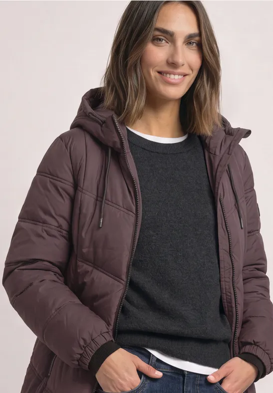 Femme portant une veste matelassée à capuche, pull et T-shirt, souriante face à l'appareil.