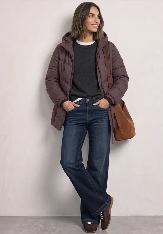 Femme en doudoune marron, pull sombre, jean évasé bleu, mocassins bruns et sac en daim