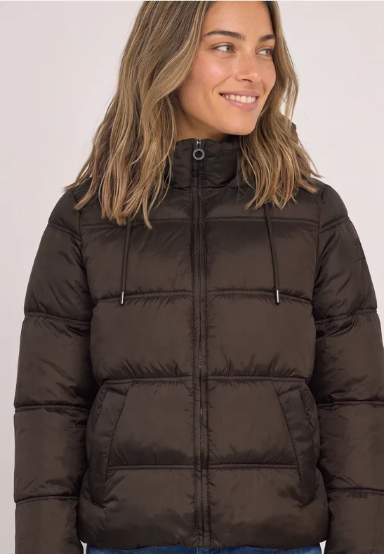 Frau in dunkelbrauner Steppjacke mit Kapuze und Reißverschluss, lächelt.