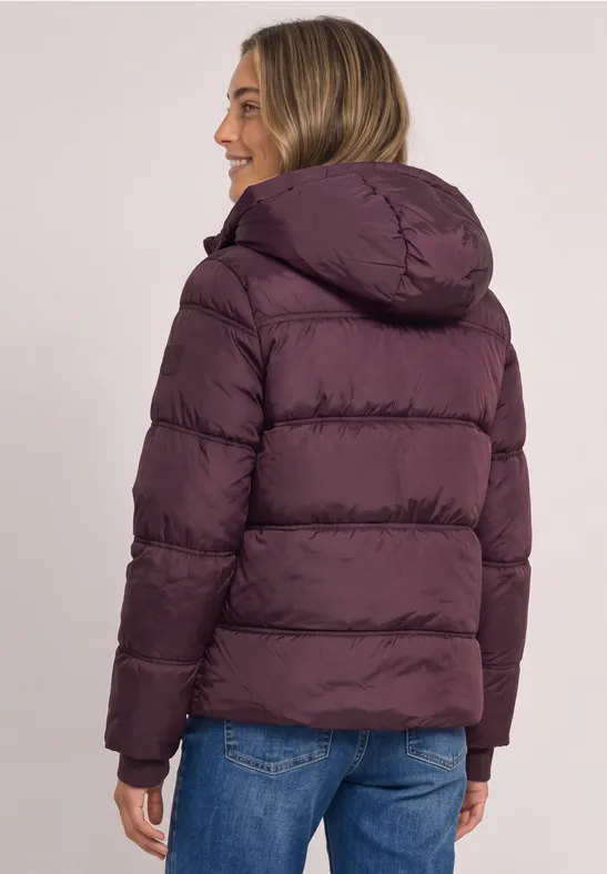 Rückenansicht einer Person in einer lilafarbenen Steppjacke mit Kapuze und Jeans.