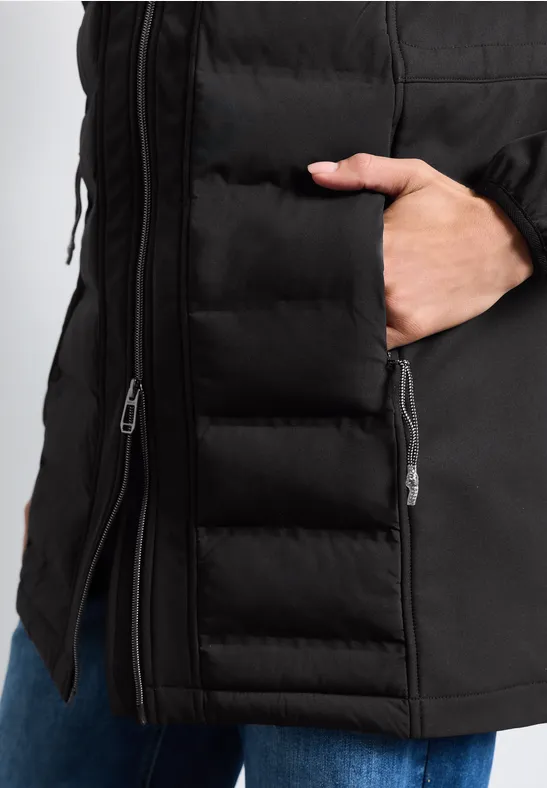 Veste matelassée noire avec poche à zip latéral et main glissée à l’intérieur.