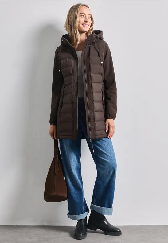 Femme en manteau matelassé marron à capuche, jean ample, bottines noires et sac marron.