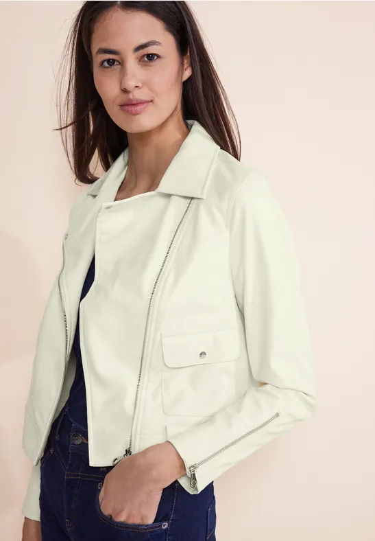 Femme en veste blanche et pantalon foncé sur un fond clair.