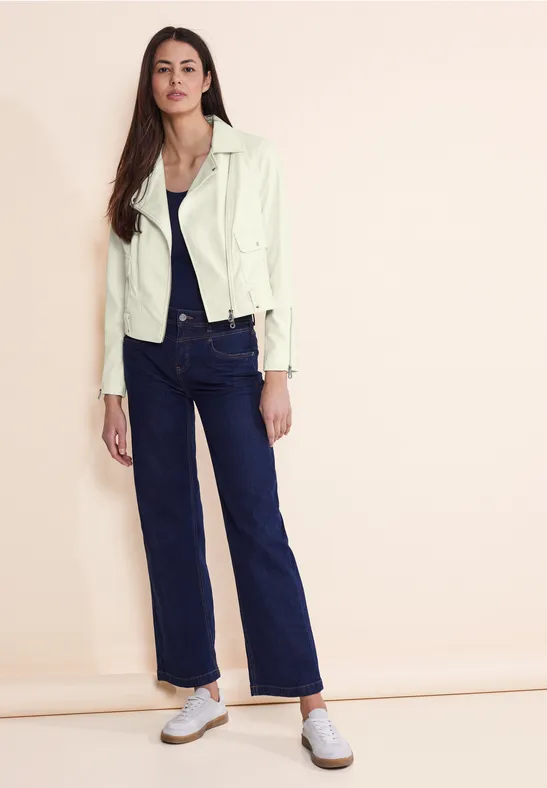 Femme en veste claire, jean bleu foncé et baskets blanches.