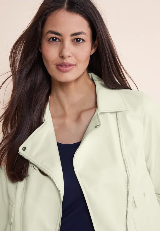Femme aux longs cheveux foncés en veste claire et haut foncé.