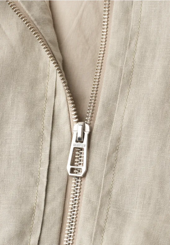 Nahaufnahme eines silbernen Reißverschlusses auf hellbeigem Stoff.