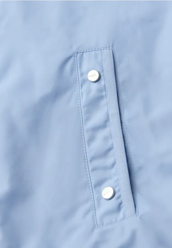 Detail einer hellblauen Jackentasche mit silbernen Druckknöpfen