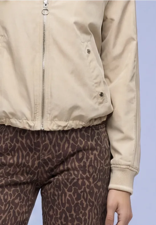 Eine Person trägt eine beige Jacke und braune, leo-gesprenkelte Leggings vor hellem Hintergrund.