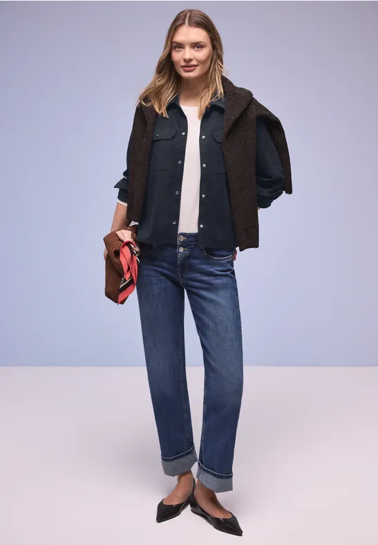 Modieuze look: zwarte jas over de schouders, witte top, blauwe jeans, bruine loafers en rode clutch.